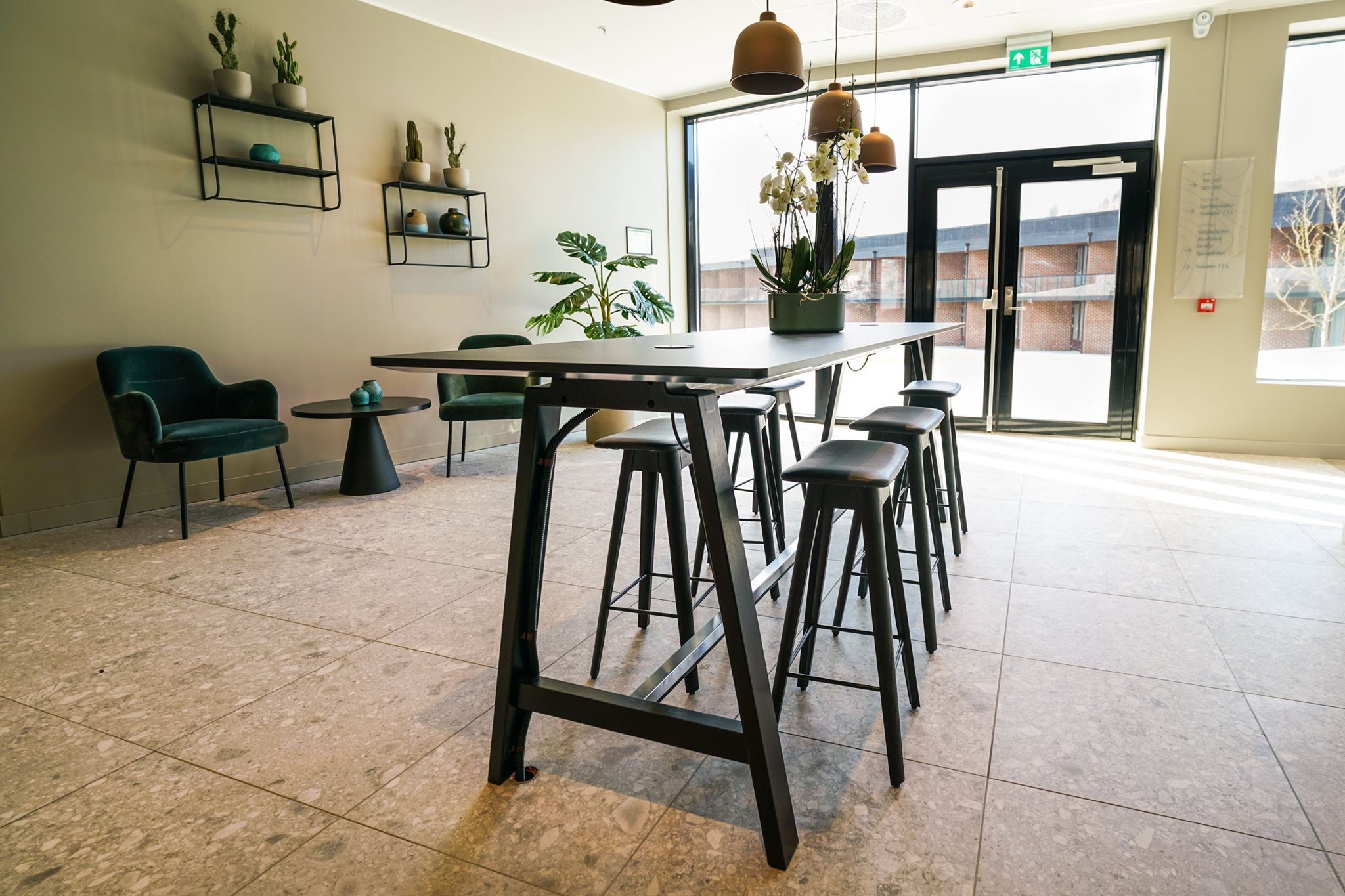 Inngangsparti med høge bord, hengande lampar og eit stilig interiør.