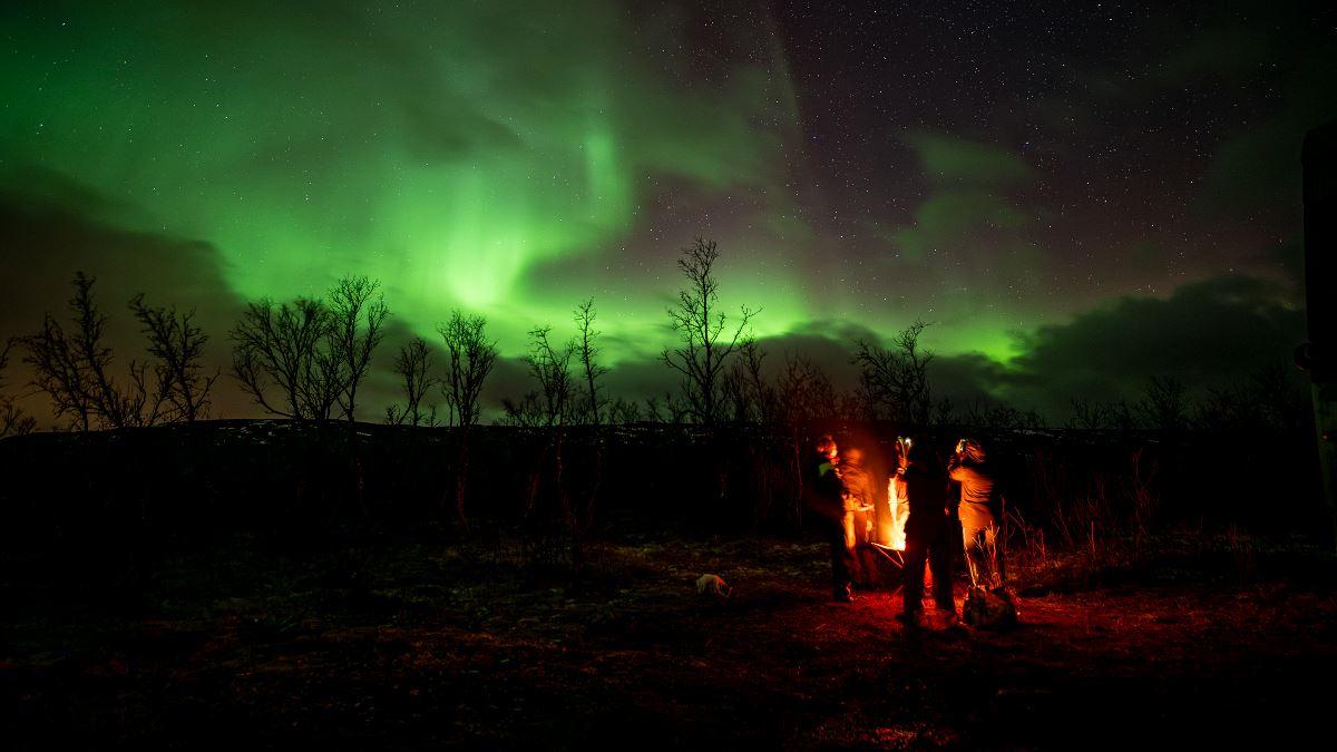 Guests around a bonfire and Northern lights