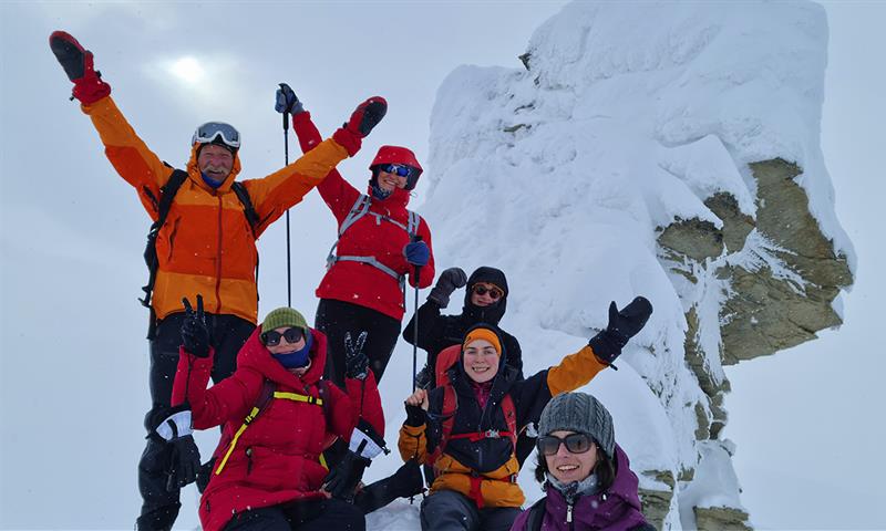 En gruppe med gjester som jubler for kameraet på toppen av Trollsteinen i snødekte omgivelser