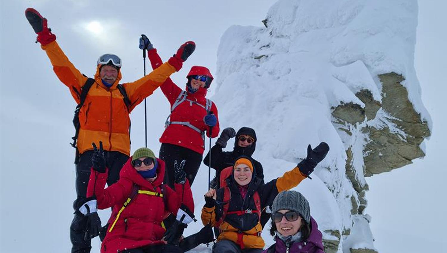 En gruppe med gjester som jubler for kameraet på toppen av Trollsteinen i snødekte omgivelser