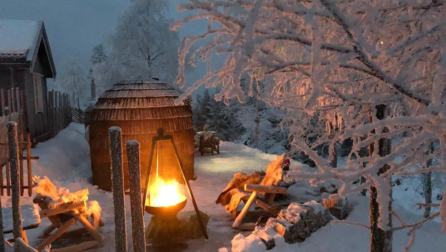 Outdoor hot tub and firepit surrounded by snow-covered trees on a winter evening.
