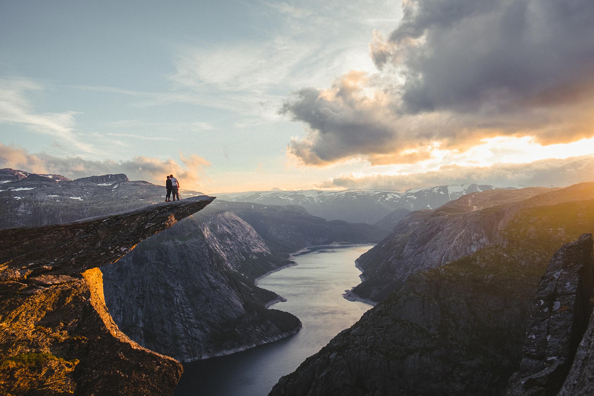 A couple standing on Trolltunga looking over Ringedalsvatnet lake. 