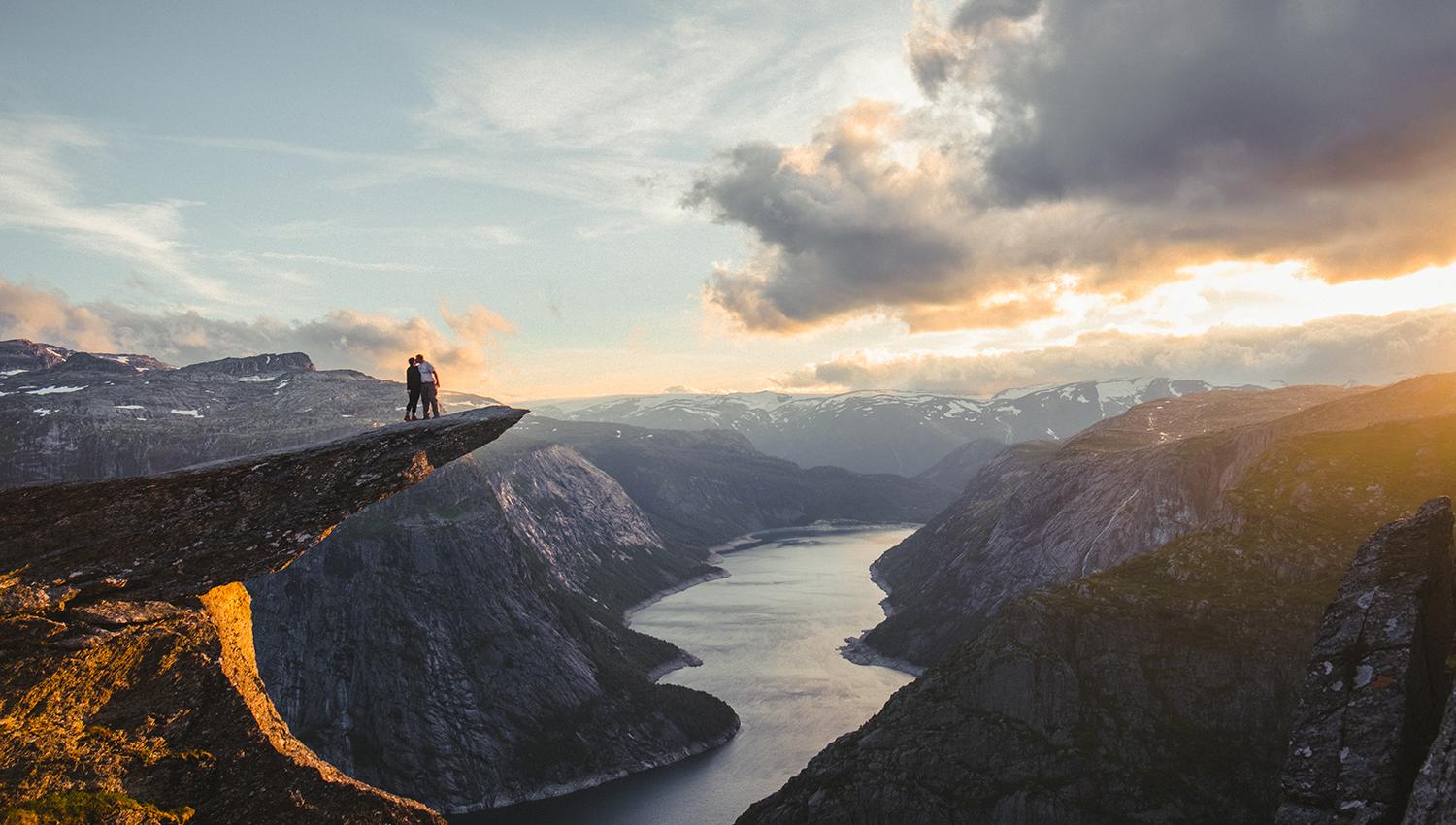 Et kjærestepar står på Trolltunga og ser utover Ringeldasvatnet.