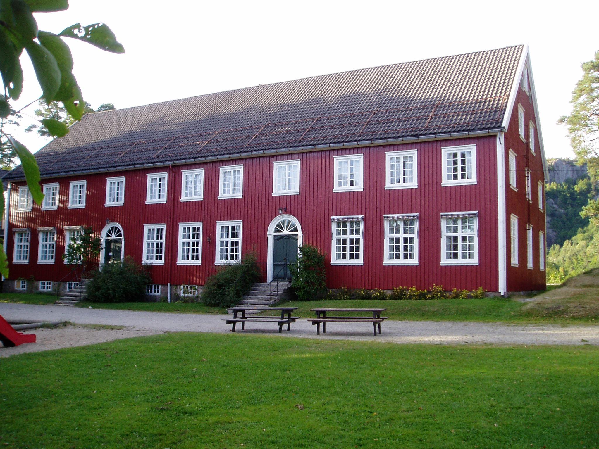 Høgtun Kultursenter, stort rødt bygning med hvite karmer. 20 vinduer på en vegg + 2 dører.