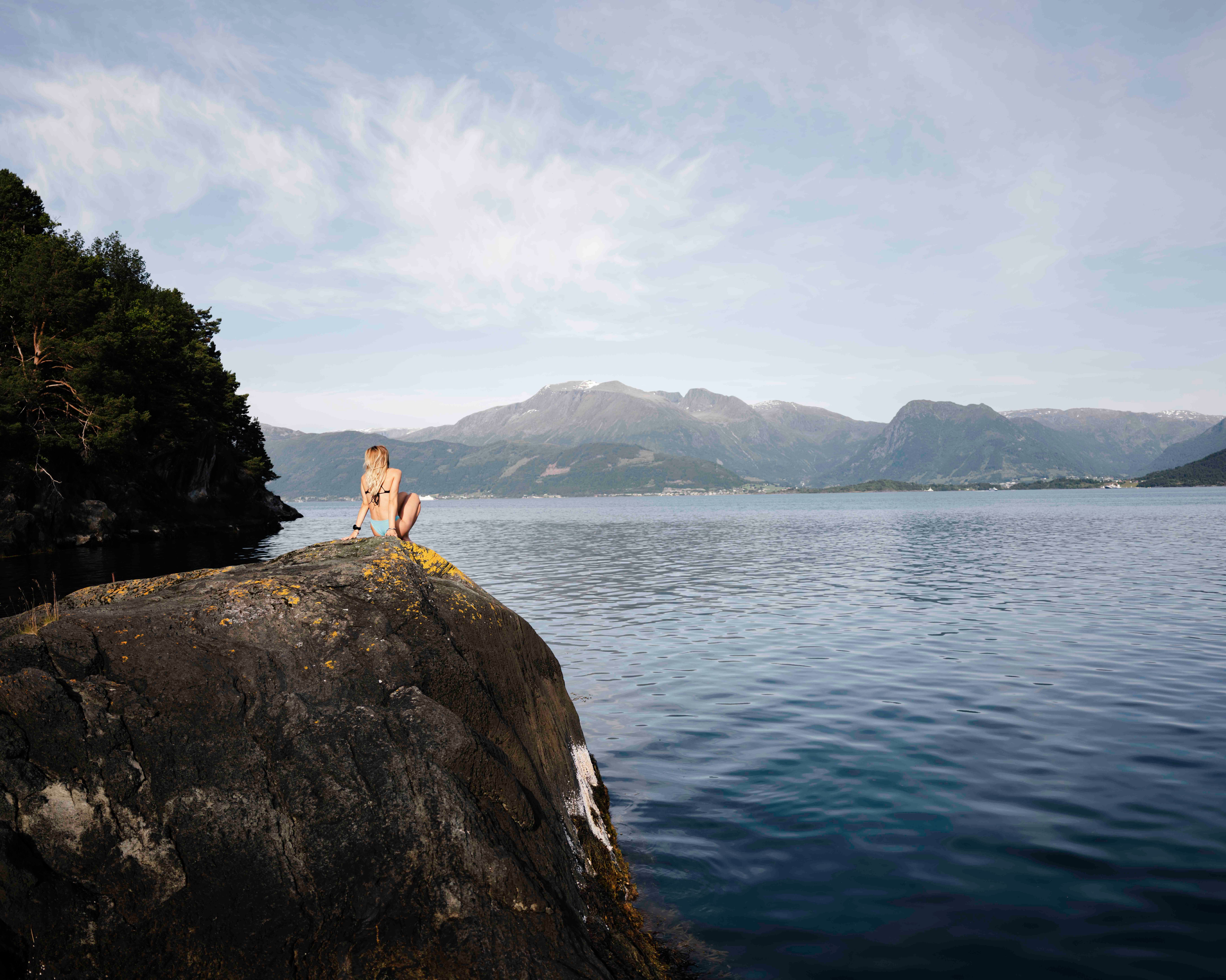 Person sit ved fjorden på svaberg med utsikt mot fjella i Hardanger.