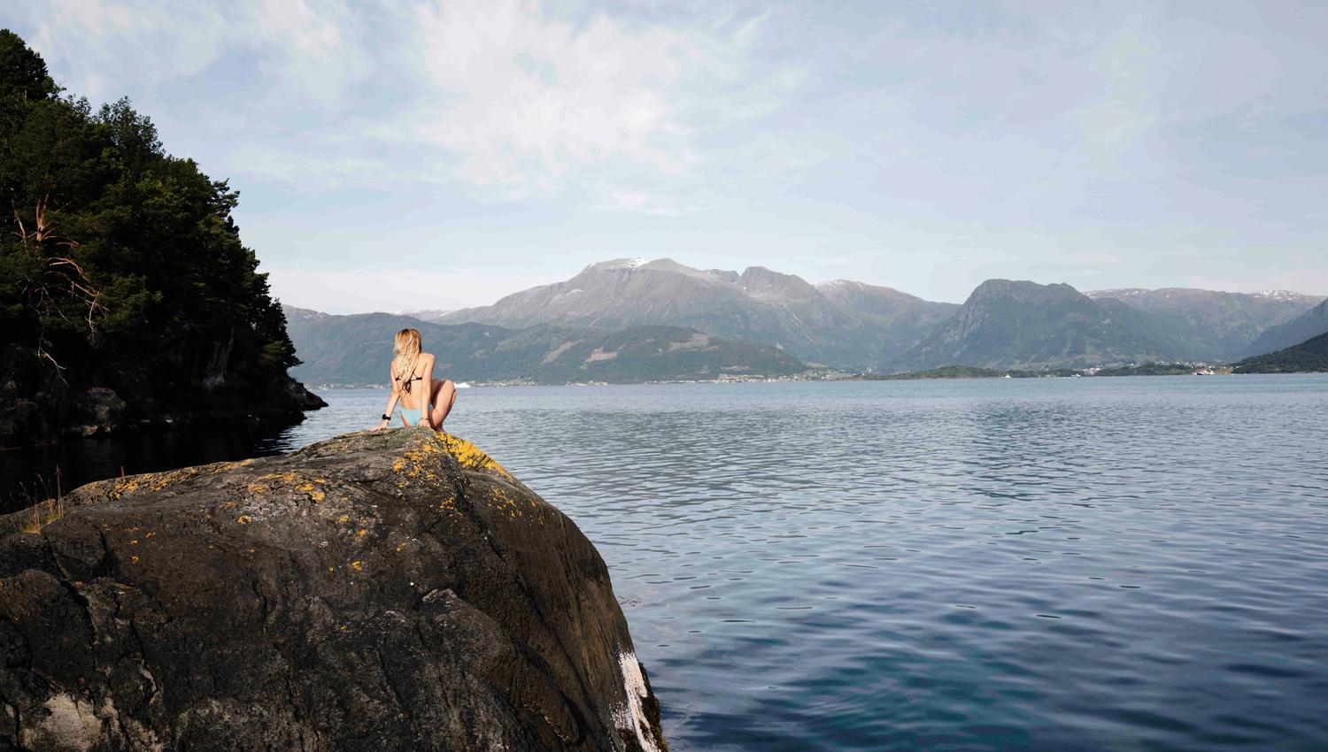 Person sit ved fjorden på svaberg med utsikt mot fjella i Hardanger.