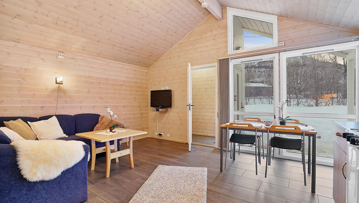 Cosy living room with blue sofa, dining table, and large windows facing snowy scenery