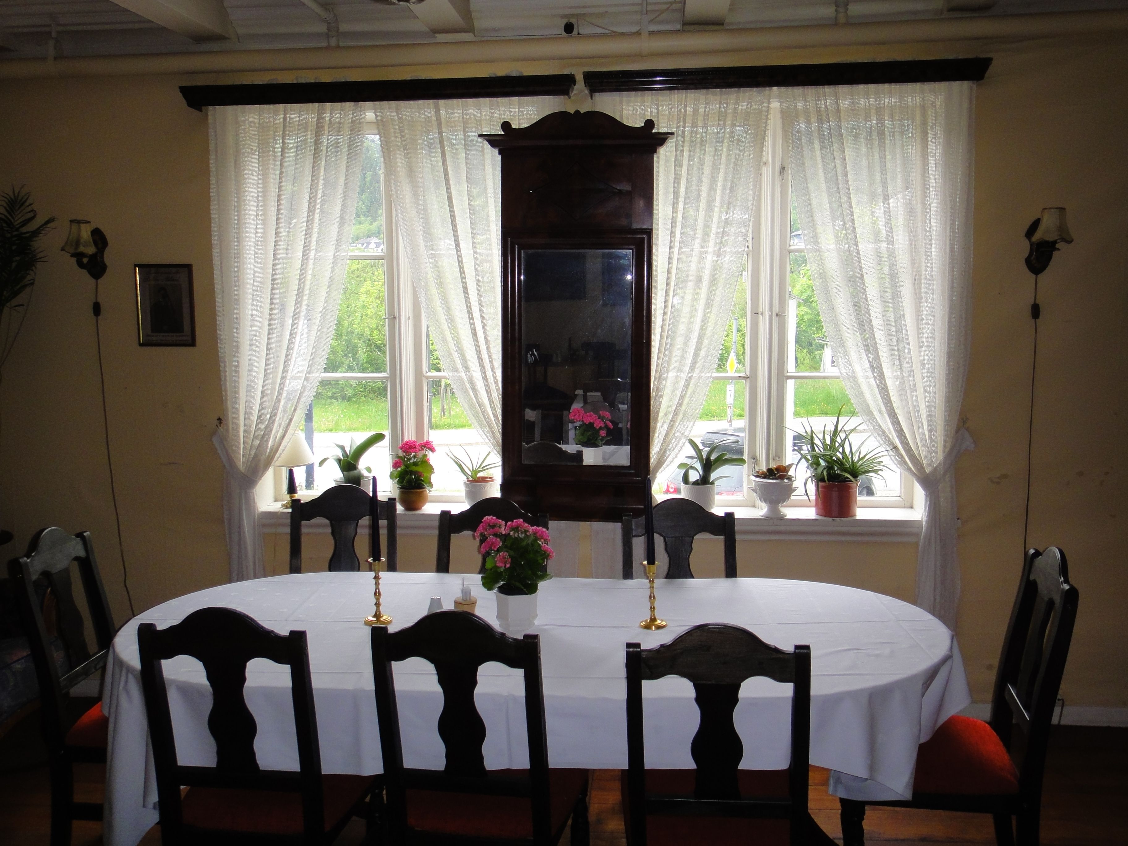 Lys og innbydande spisestove med kvit duk, gamle stolar og utsikt mot hagen på Jaunsen Gjestgjevarstad i Hardanger.