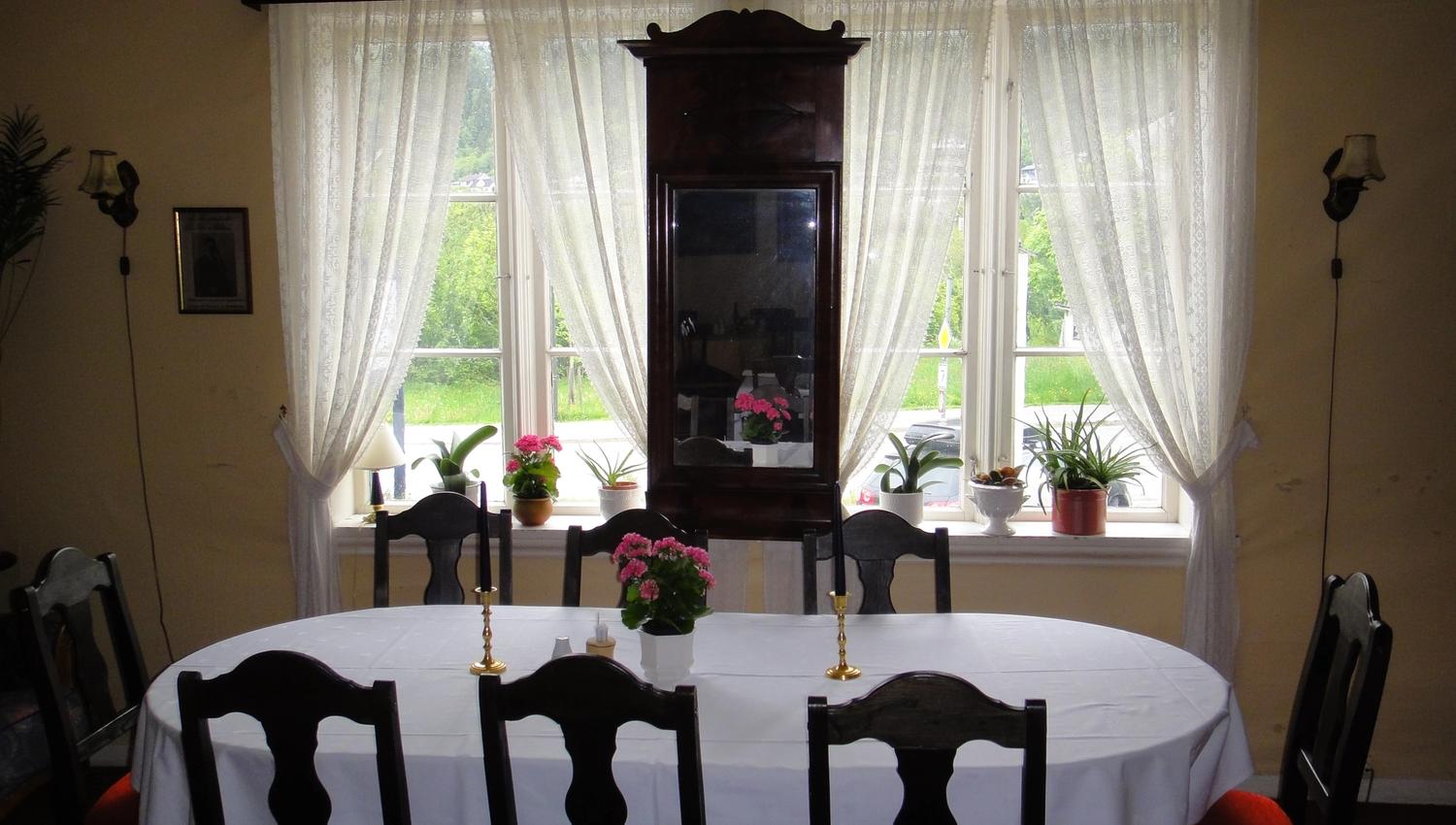 Bright and inviting dining room with white tablecloth, antique chairs and garden view at Jaunsen Guesthouse in Hardanger, Norway.
