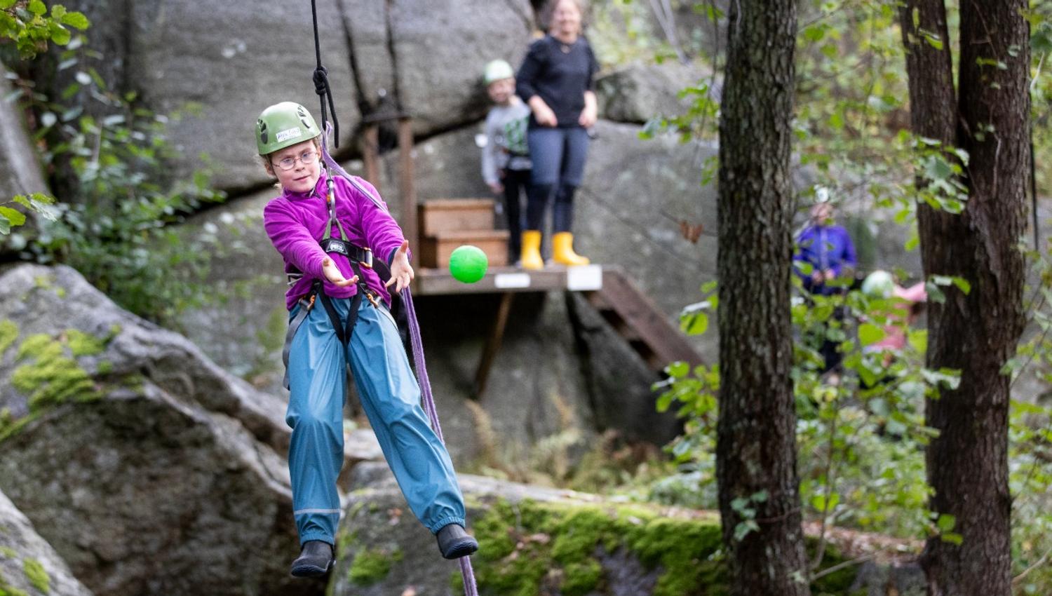 En jente henger i et tau samtidig som hun kaster ball
