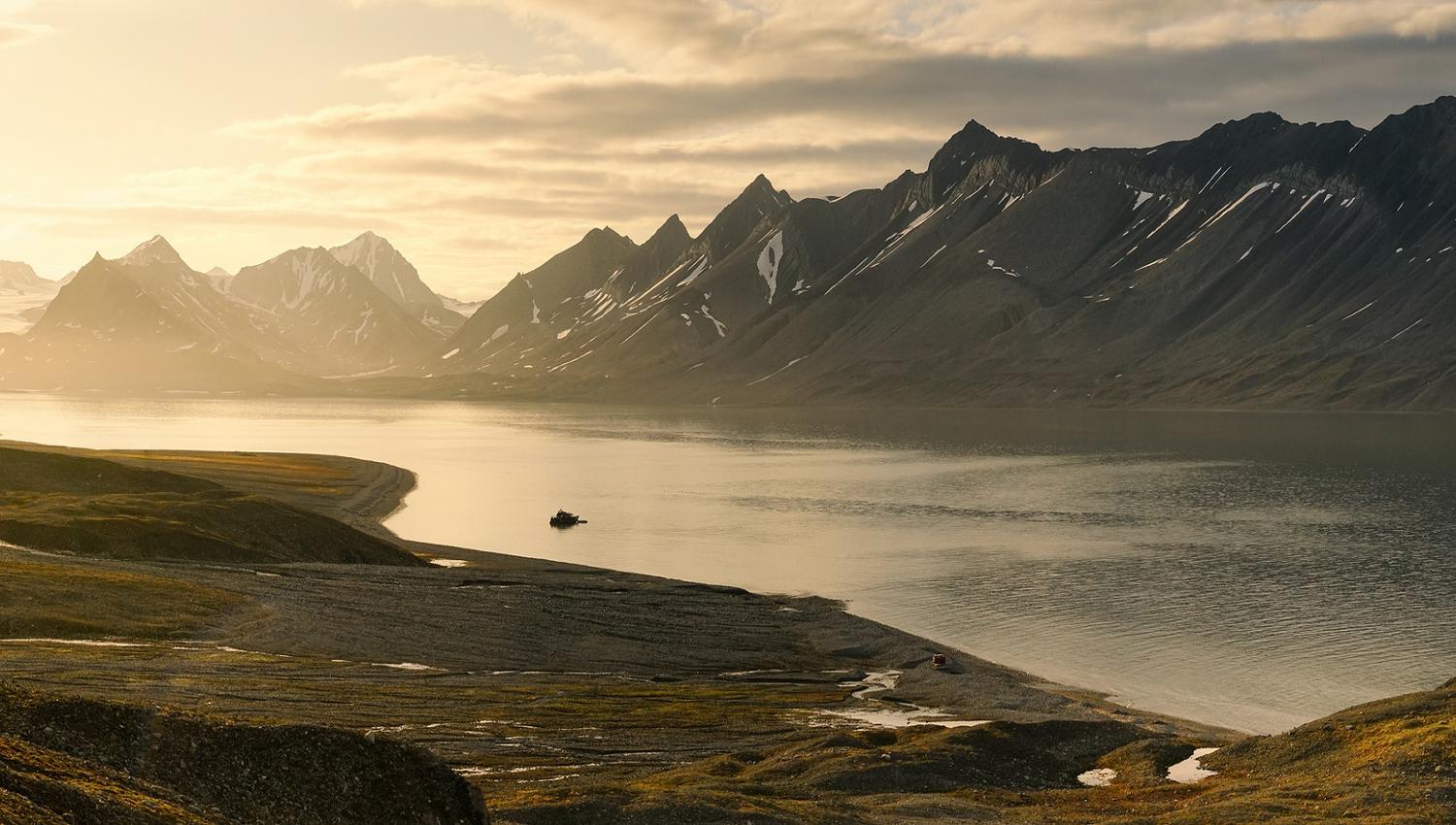 A boat floating in a calm fjord with a mountainous landscape in the background