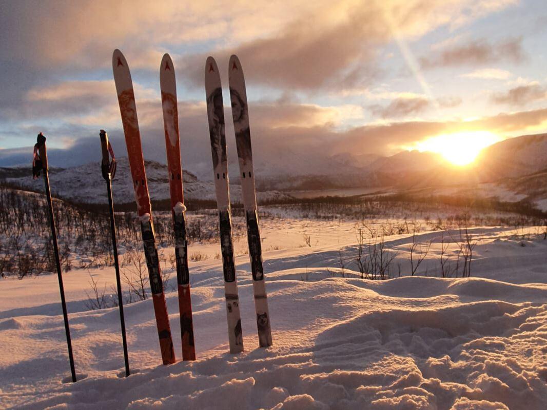 Skis and poles sit ready in the snow while the sun shines bright behind