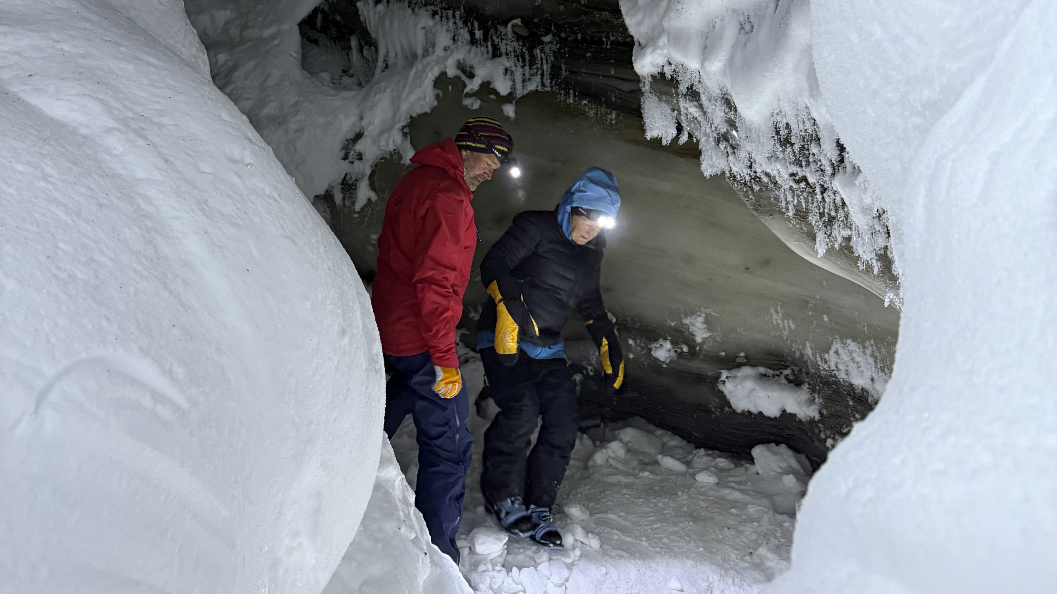 Two people standing inside a ice cave with head lamps on