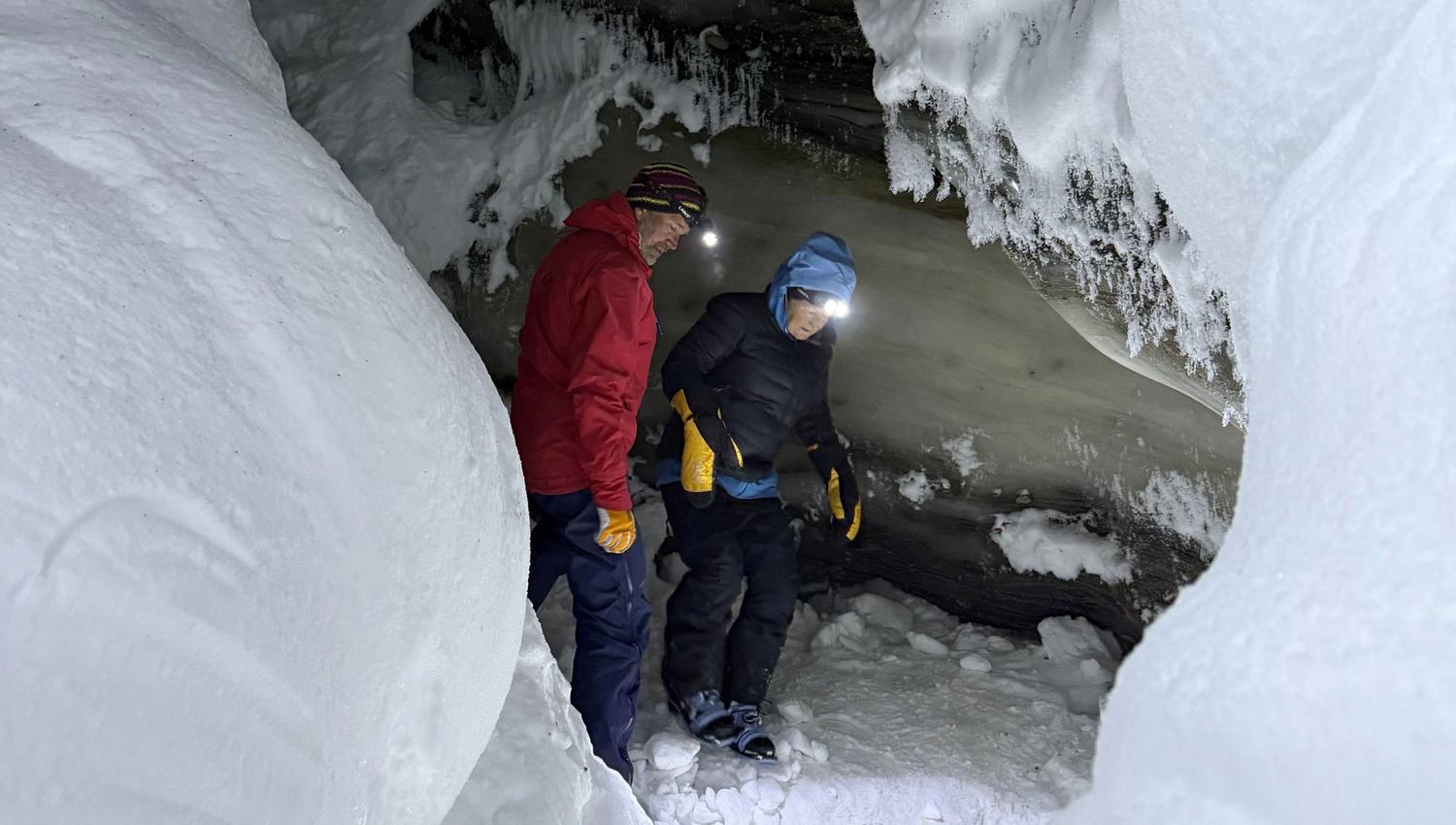 Two people standing inside a ice cave with head lamps on