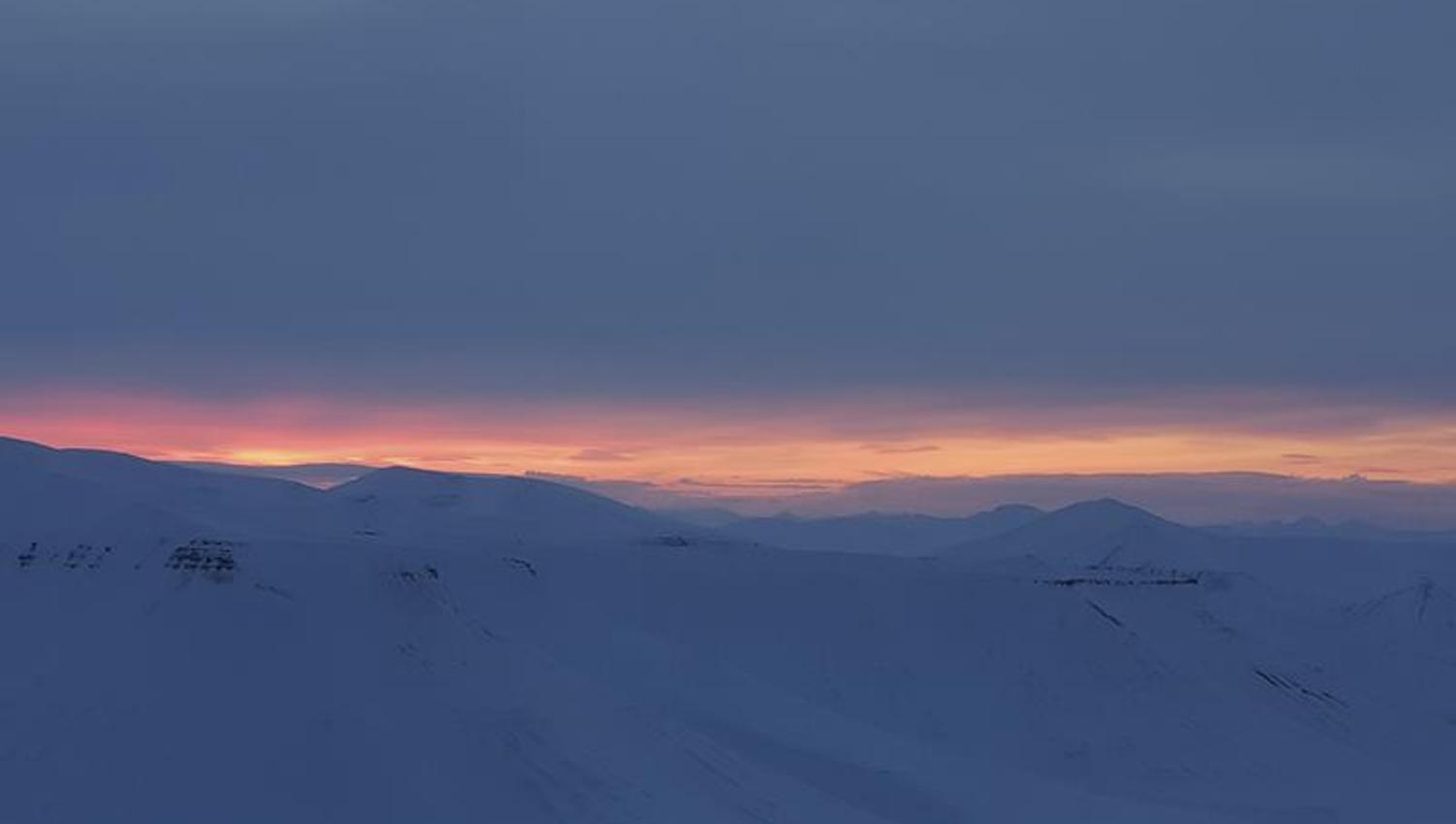 Et snødekt landskap med lave skyer og en tynn stripe med lys fra en solnedgang fjernt i bakgrunnen