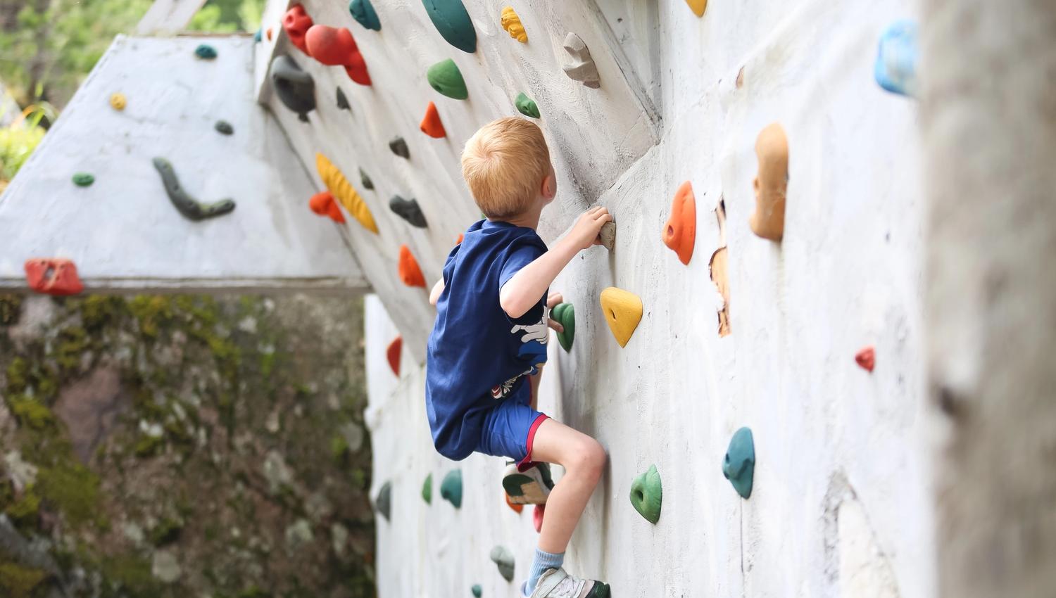 A child climbing on a wall with colorful climbing holds.