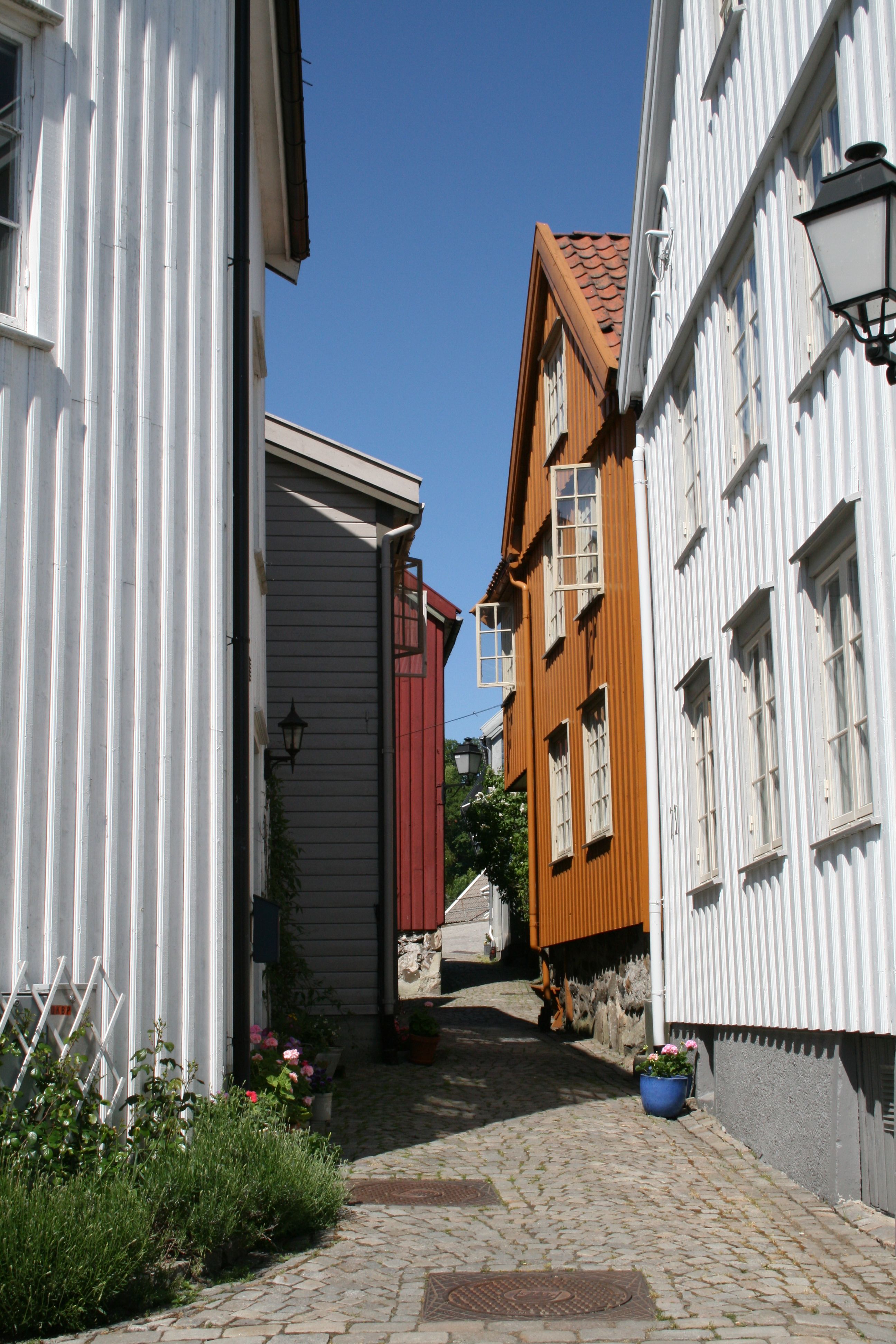 Det smale smuget på Øvre Tyholmen i Arendal med gamle hvite, rød og okerfargede trehus tett i tett med en smal brosteinsbelagt gate i mellom.