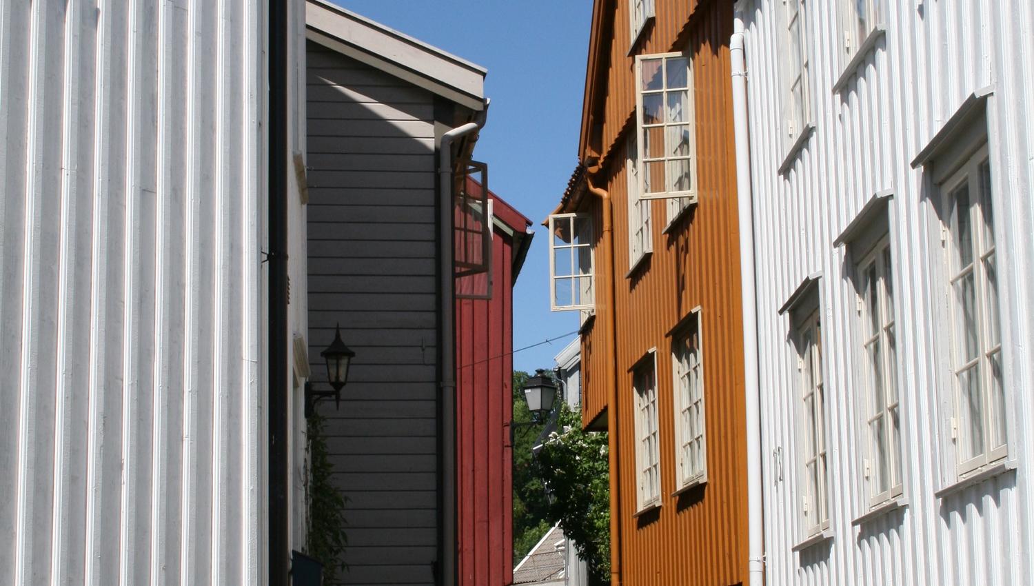 Det smale smuget på Øvre Tyholmen i Arendal med gamle hvite, rød og okerfargede trehus tett i tett med en smal brosteinsbelagt gate i mellom.