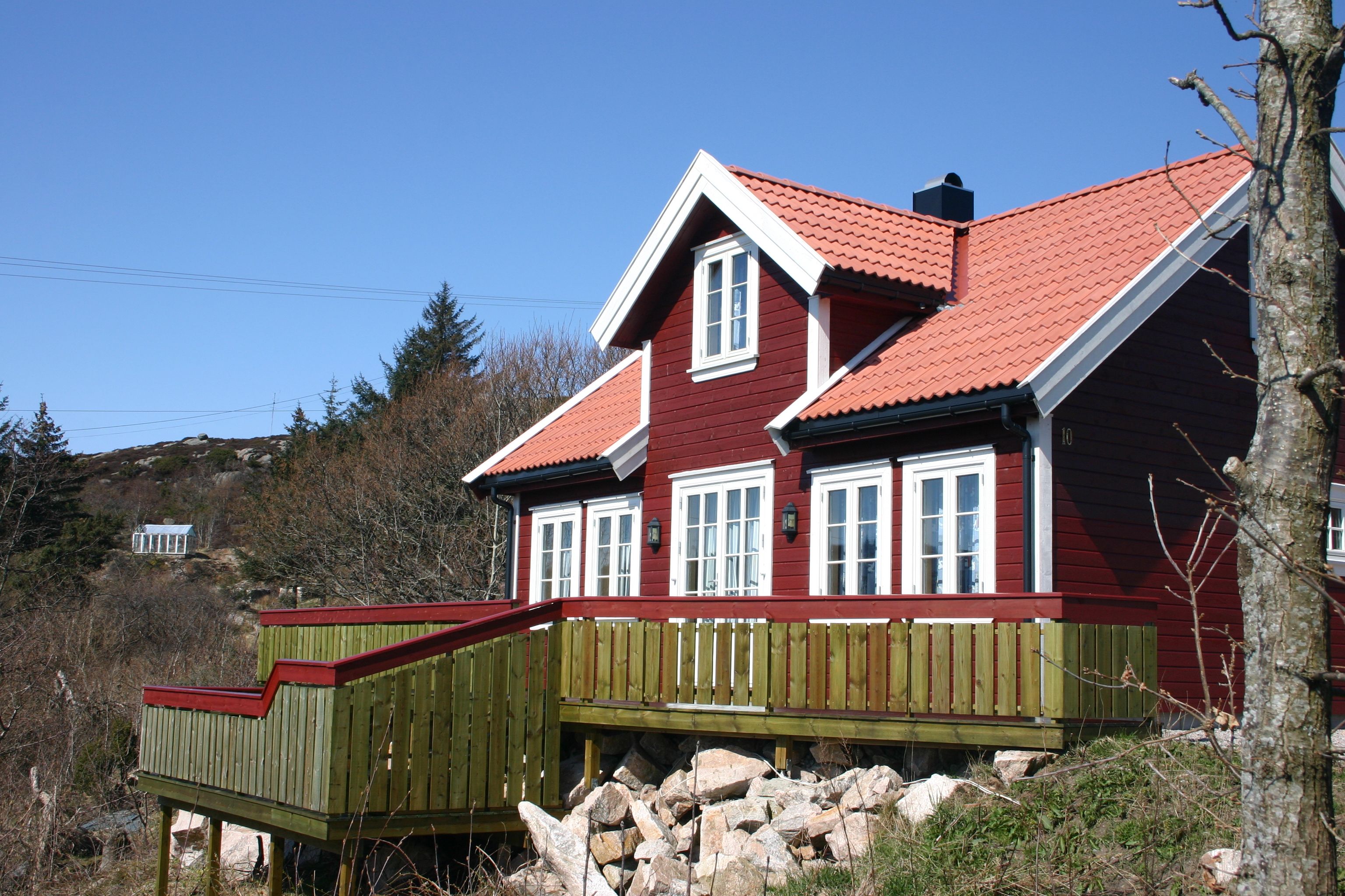Lindesnes Camping og Hytteutleie - En stor rød hytte med hvite karmer, med grønn terrasse