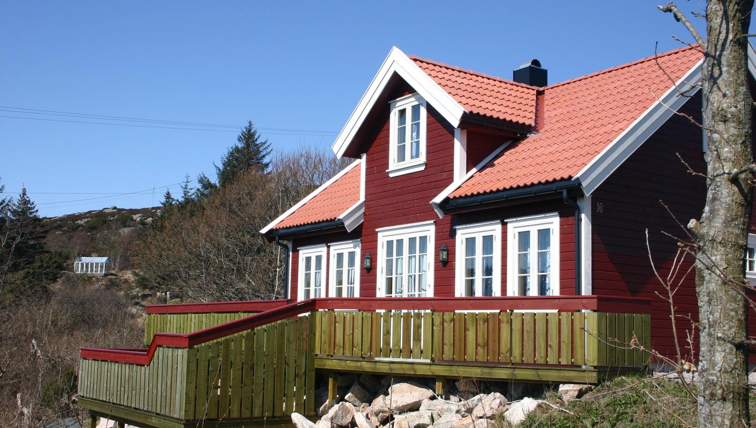 Lindesnes Camping og Hytteutleie - En stor rød hytte med hvite karmer, med grønn terrasse