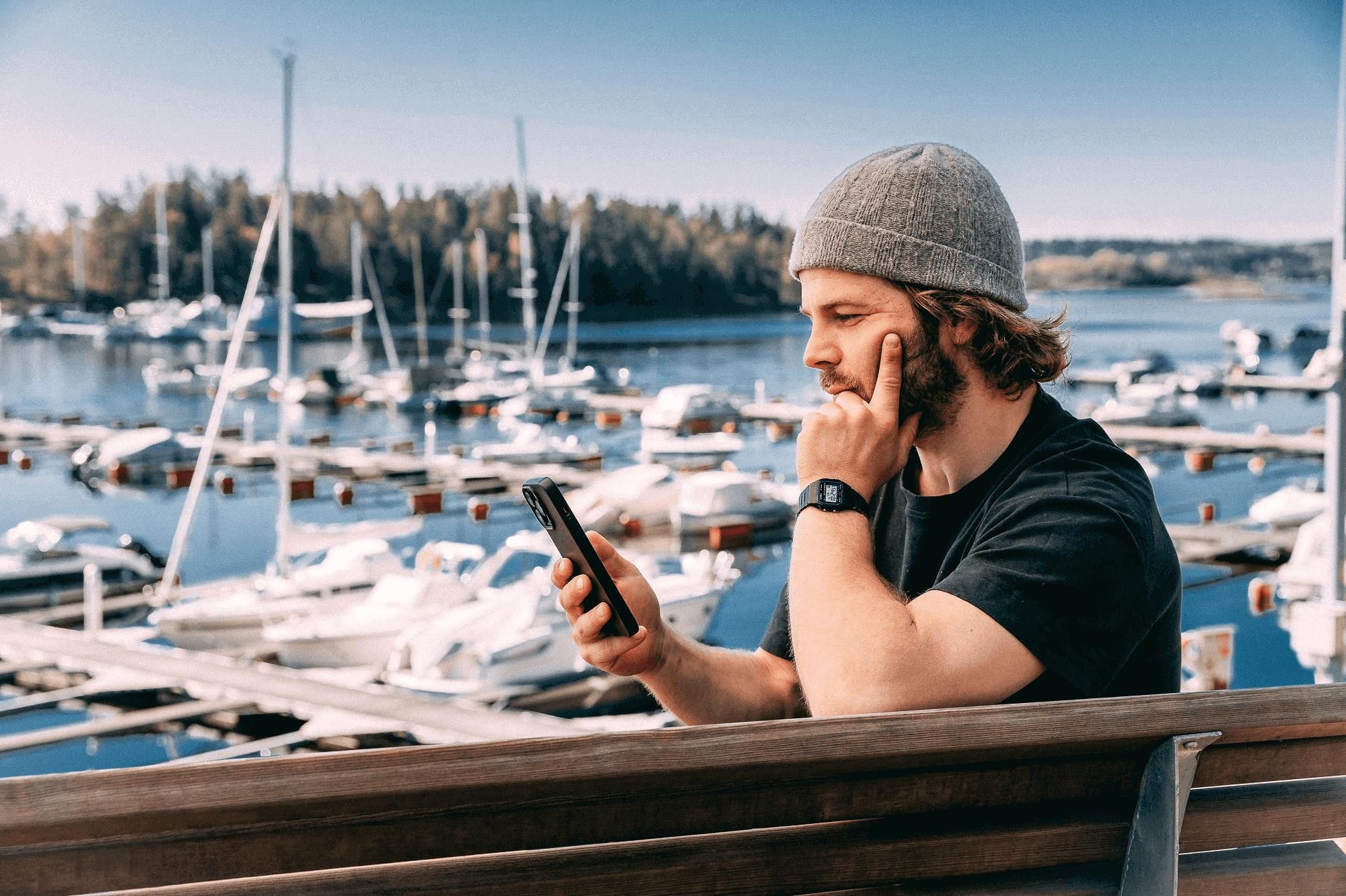 Mann som ser på telefonen foran marina med mange båter