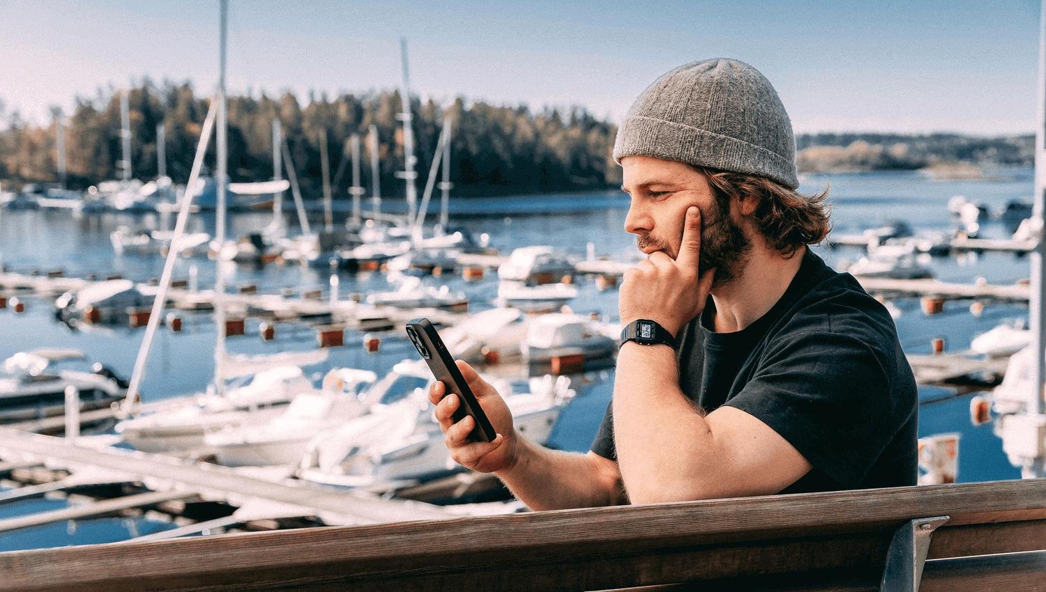 Mann som ser på telefonen foran marina med mange båter