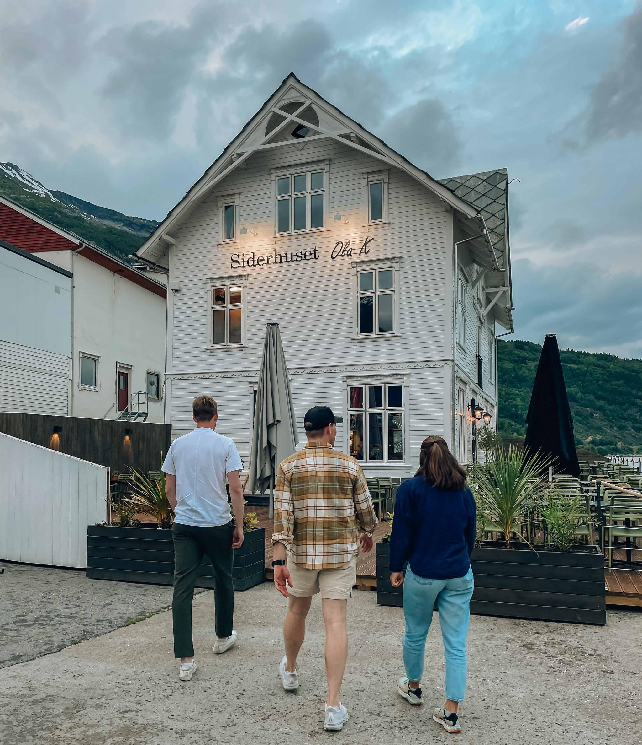 Three people walking towards Siderhuset Ola K, a charming restaurant in Hardanger, surrounded by fjords and mountains.
