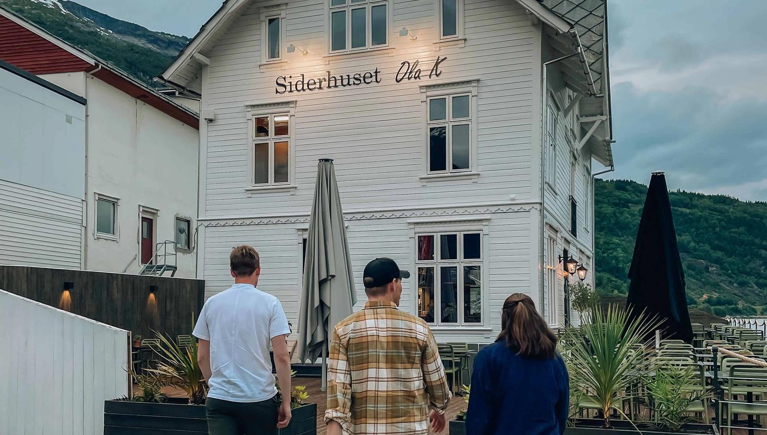 Three people walking towards Siderhuset Ola K, a charming restaurant in Hardanger, surrounded by fjords and mountains.
