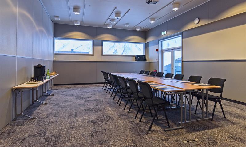 Et konferanserom med langbord, stoler og servering