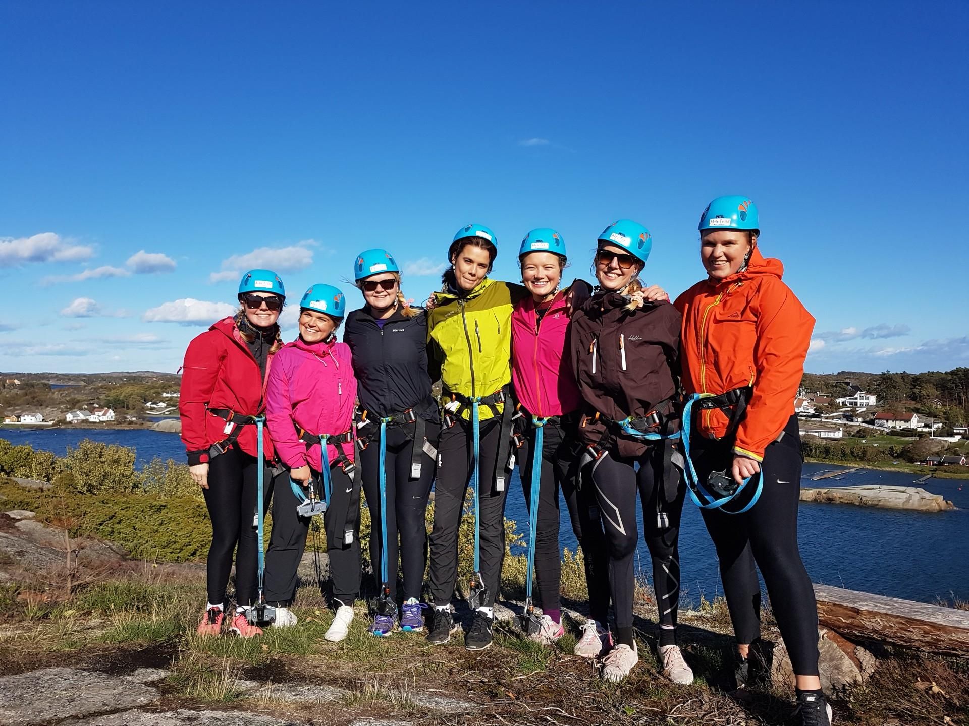 En blid jentegjeng på 7 står på toppen av fjellet med skjærgården i bakgrunnen klare til å rappellere