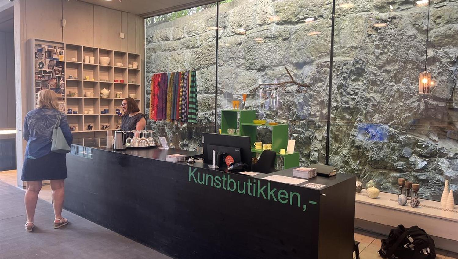 Resepsjonsområde i kunstbutikken med disk, glassvegg og utstilte varer.