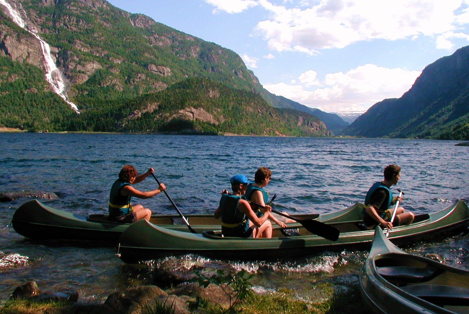 Familie på kanotur på fjorden med foss og grøne fjell i bakgrunnen.