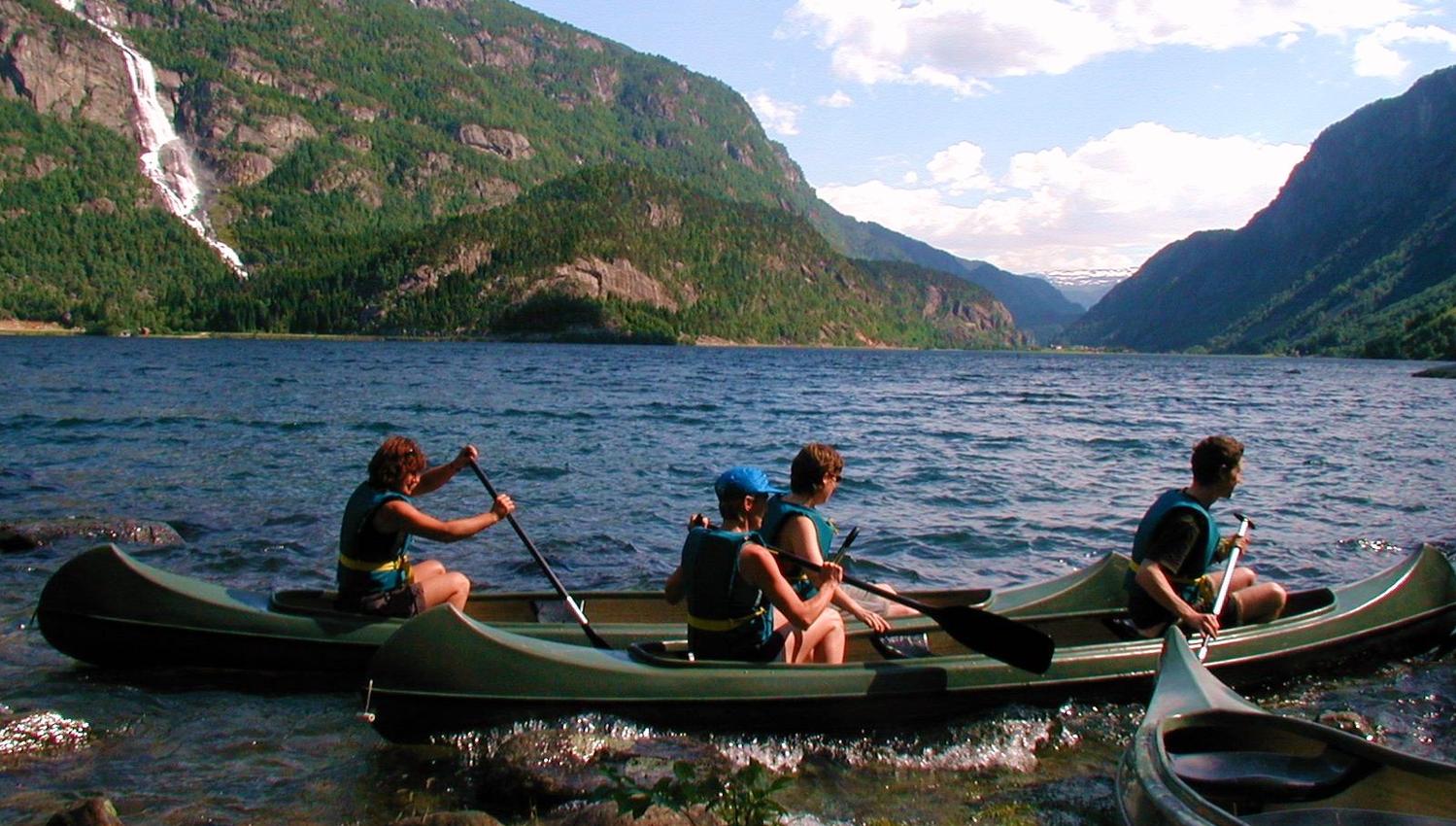 Familie på kanotur på fjorden med foss og grøne fjell i bakgrunnen.