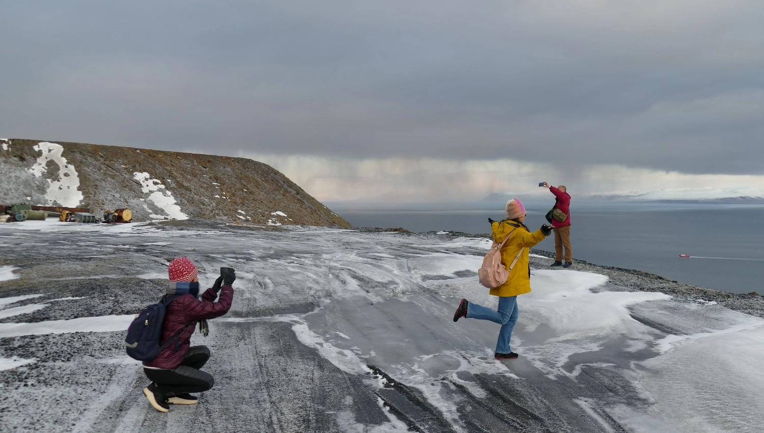 Three people posing to take a photo on snowcovered grounds with a mountain and the ocean in the background