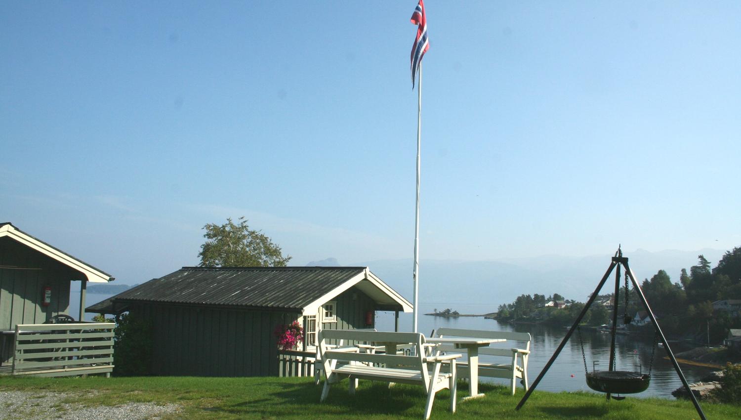 Utsikt frå Oddland Camping i Hardanger med hytter, flaggstong og fjordutsikt ein solrik sommardag.