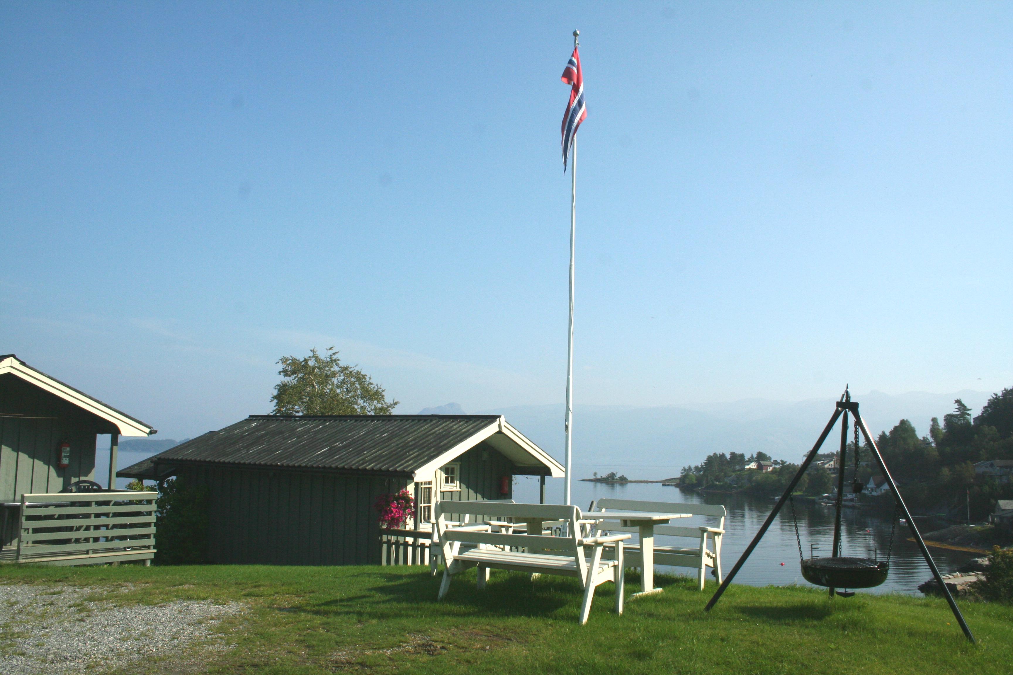 View from Oddland Camping in Hardanger with cabins, a flagpole, and stunning fjord scenery on a sunny summer day.