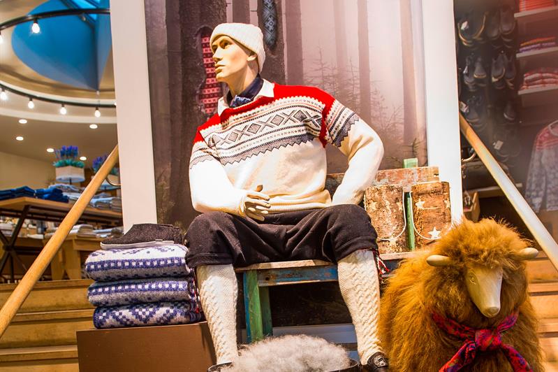 Utstillingsdukke med genser på, en dukke av en sau, og brettede gensere.