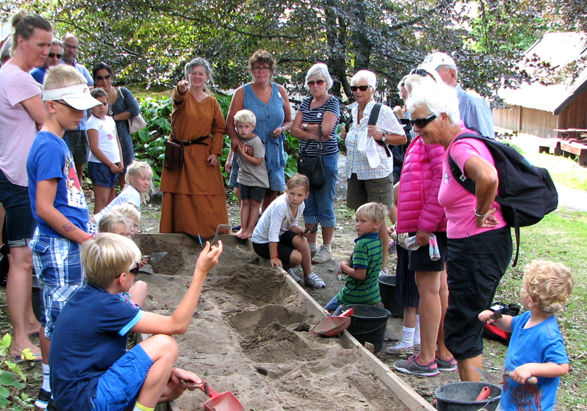 Children and adults stand around a sandbox and dig out objects from the Viking Age.