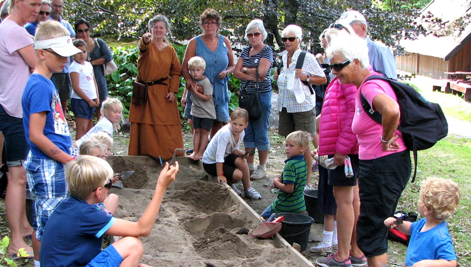 Children and adults stand around a sandbox and dig out objects from the Viking Age.