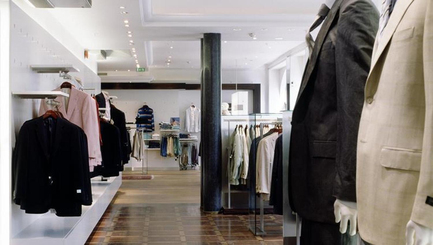 Butikkinteriør. To utstillingsdukker kledd i dress, en rekke klær som henger langs veggene.