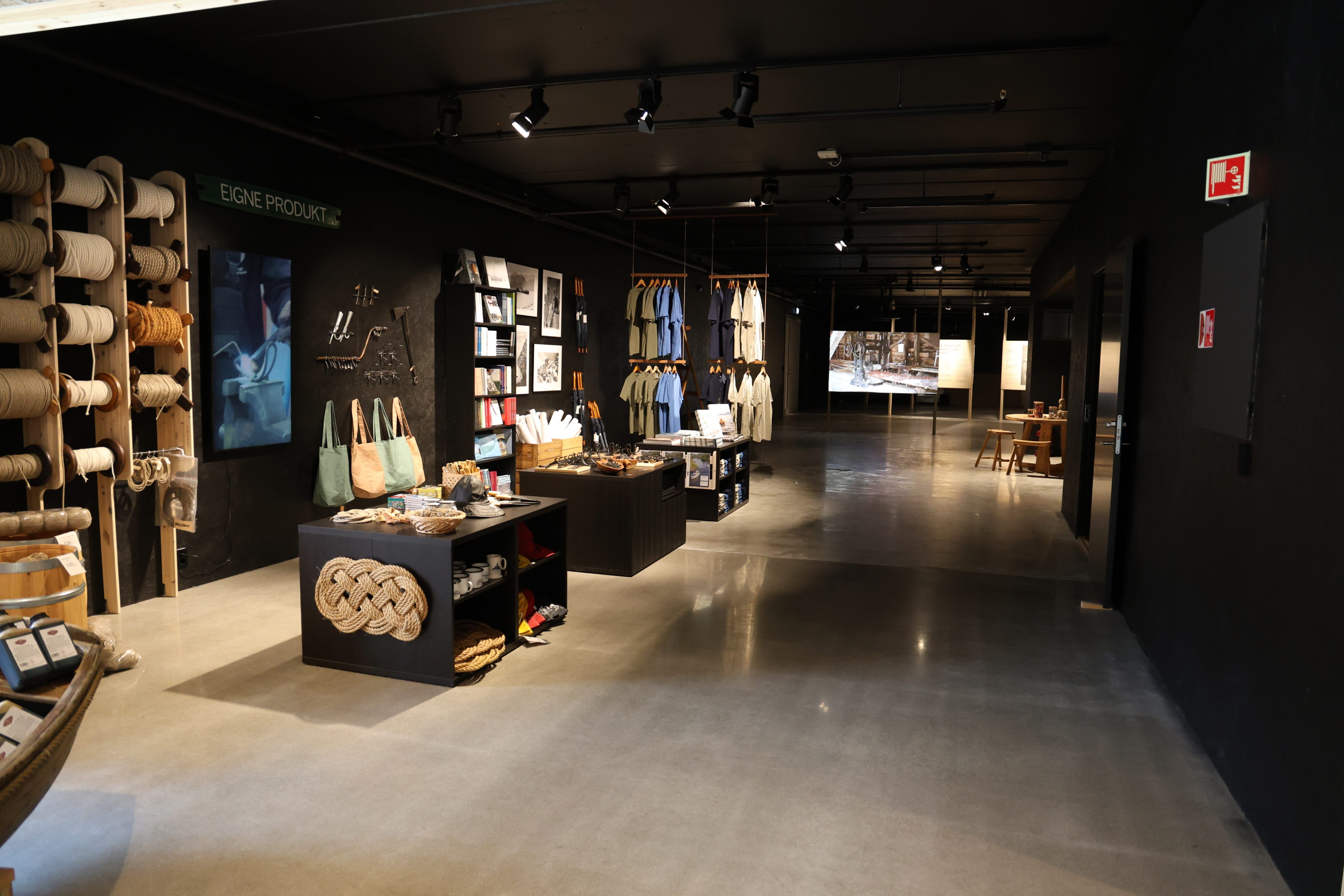 Museum shop with many items on display. A wall with ropes on spools and forged products. T-shirts are displayed at the back of the room.