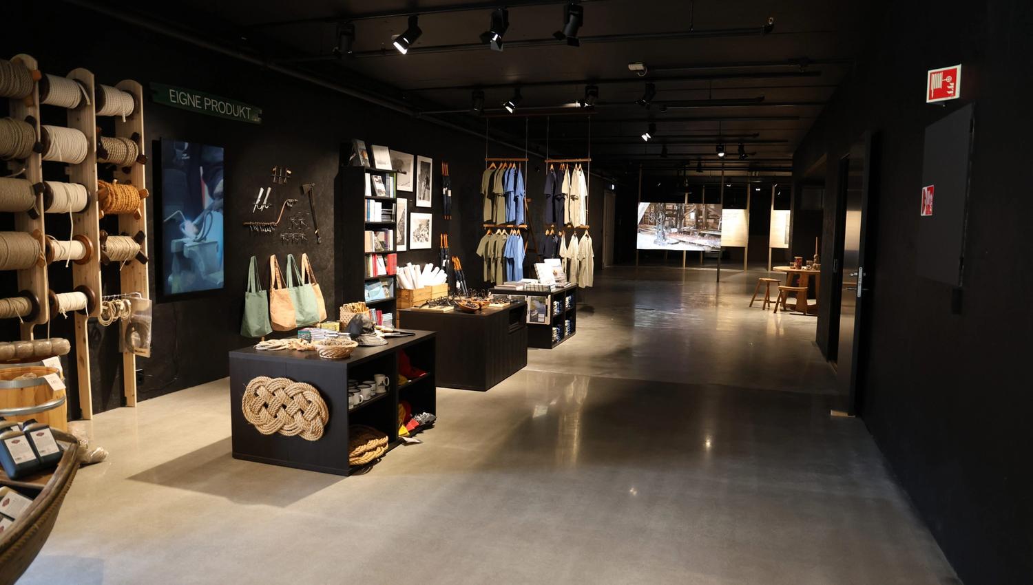 Museum shop with many items on display. A wall with ropes on spools and forged products. T-shirts are displayed at the back of the room.