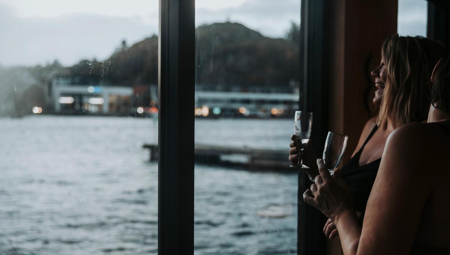 To damer som koser seg med noe godt i glasset i badstubåten Pysen