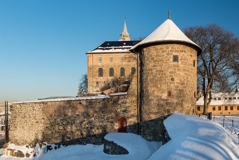 Vinterbilde av Munks tårn med slottet i bakgrunnen. Snø på bakken.