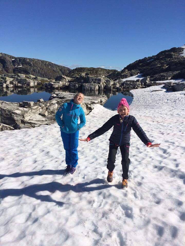 To jenter smiler og leikar på ei snøfonn ved Hallet grøne på Hardangervidda.