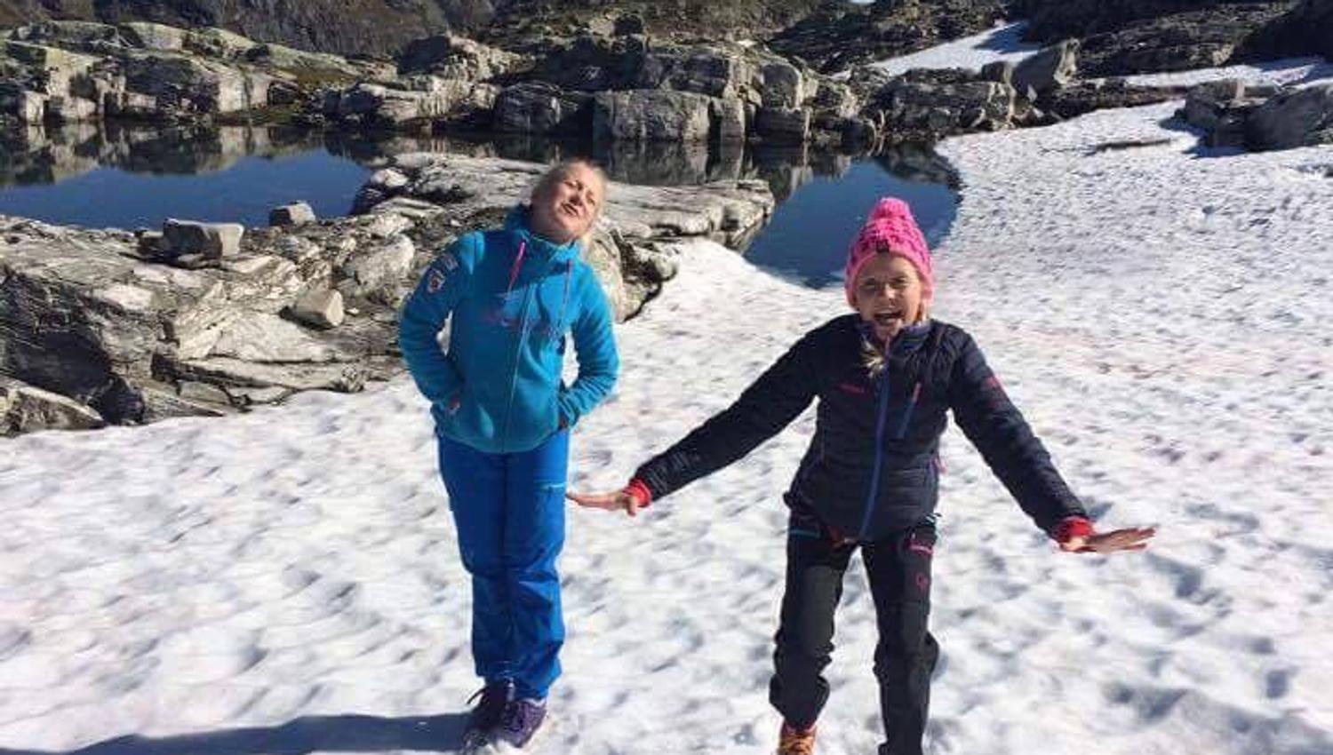 To jenter smiler og leikar på ei snøfonn ved Hallet grøne på Hardangervidda.