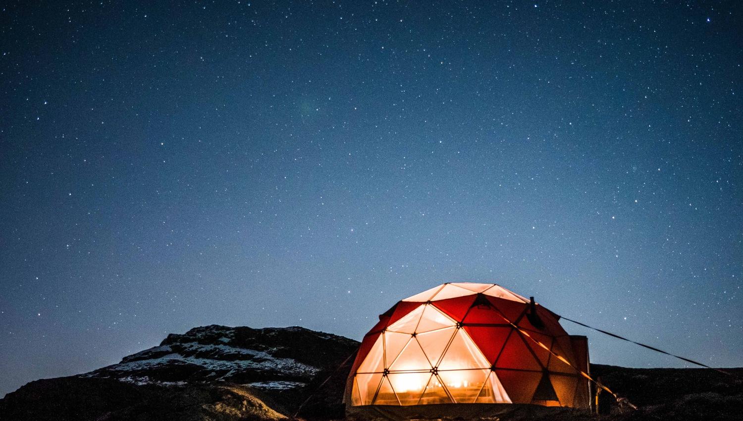 Oppvarma geodome lyser varmt i vinterlandskapet ved Trolltunga under klar nattehimmel.