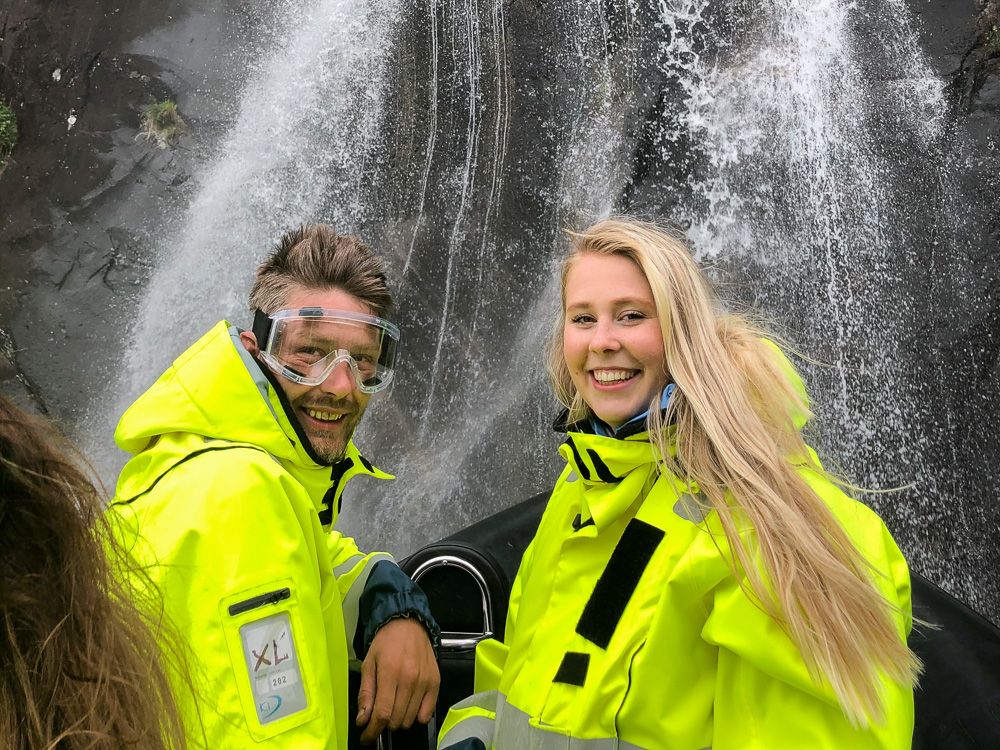 Smilande passasjerar i gule redningsdrakter nyt ei frisk oppleving under ein foss på RIB-safari i Hardanger.