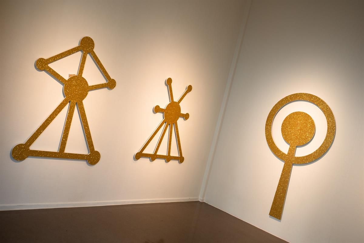 Kunstutstilling Kunstbanken - Gule veggskulpturer med grafiske, symbolske former i utstillingsrom.