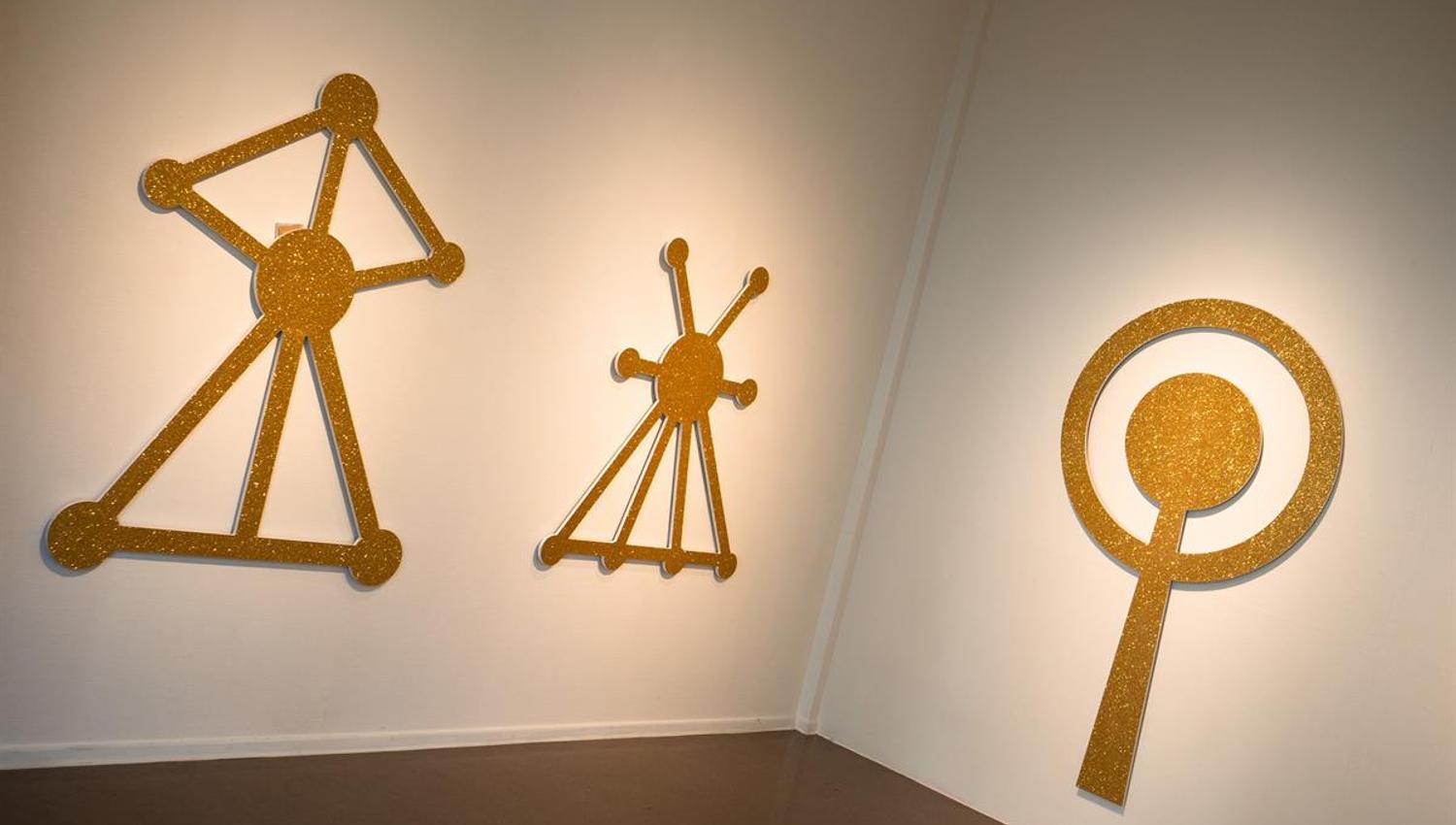 Kunstutstilling Kunstbanken - Gule veggskulpturer med grafiske, symbolske former i utstillingsrom.